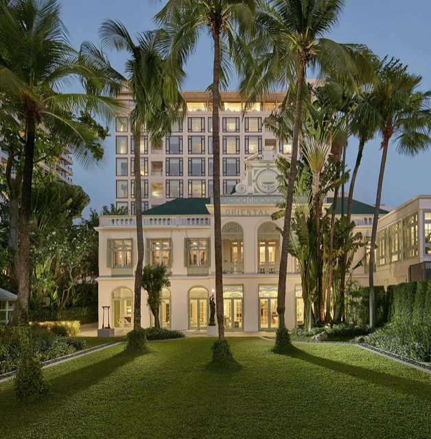 A luxury hotel exterior featuring a grand multi-story building surrounded by palm trees and lush greenery, captured during dusk.