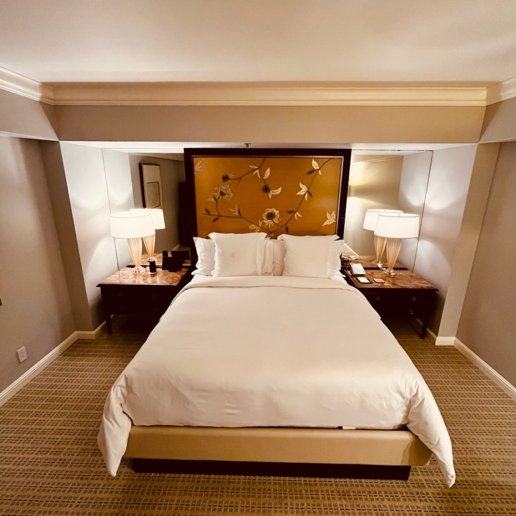 A beautifully decorated hotel room featuring a large bed with white linens, bedside tables with lamps, and an elegant floral headboard.