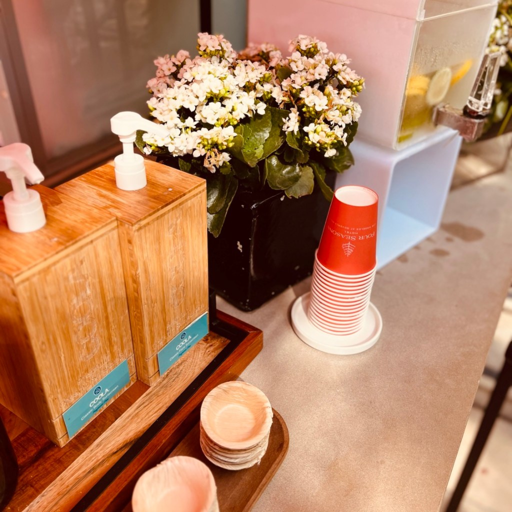 Display of hand sanitizers and eco-friendly cups alongside fresh flowers in a hotel lobby.
