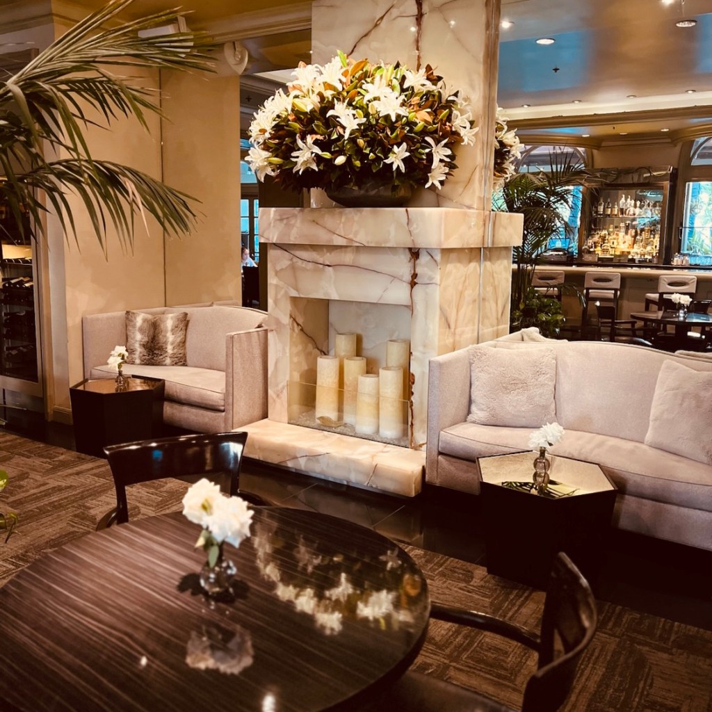 An elegantly designed hotel lounge featuring plush seating, a stylish marble fireplace with decorative candles, and vibrant floral arrangements.