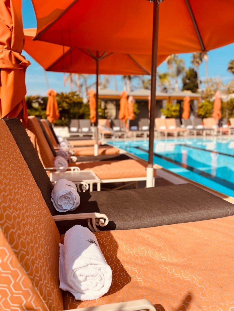 Lounge chairs by the pool at the Four Seasons Hotel Los Angeles, featuring orange umbrellas and neatly rolled white towels.