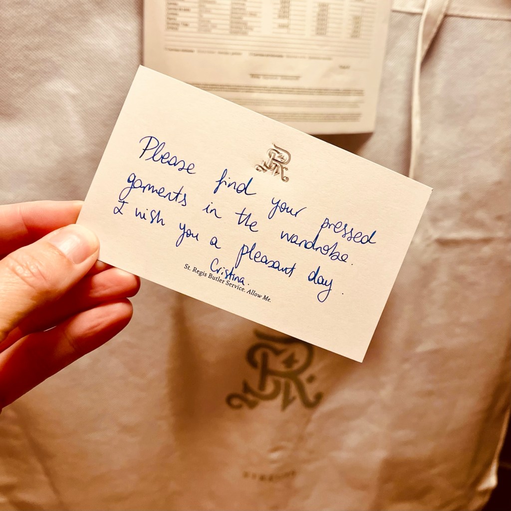 A handwritten note from the St. Regis Butler Service, indicating where pressed garments can be found, displayed against a backdrop of hotel amenities.