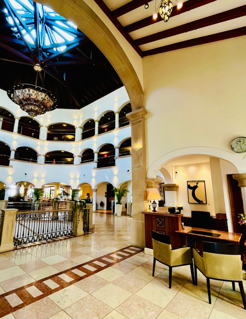 Interior of a luxury hotel lobby with high ceilings, decorative chandelier, and elegant design elements, including arches and marble flooring.