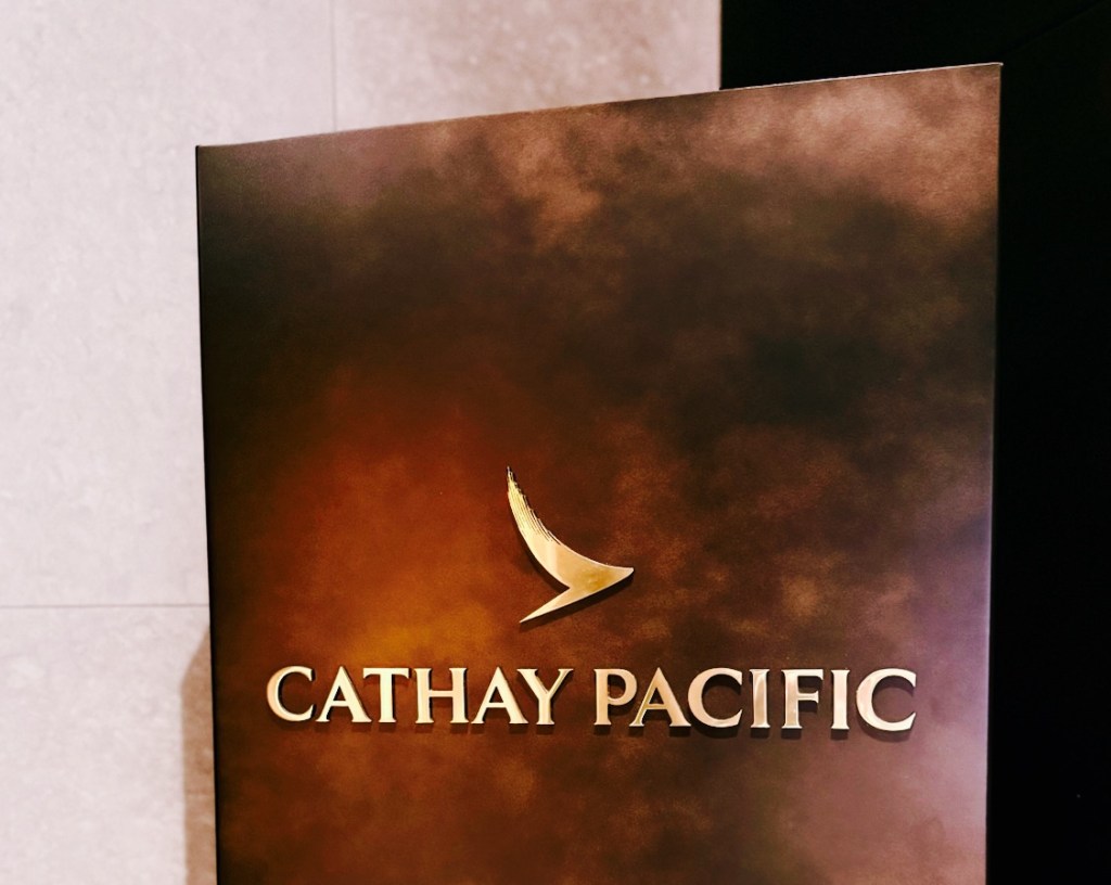 Close-up of the Cathay Pacific lounge sign, featuring a golden logo on a dark textured background.