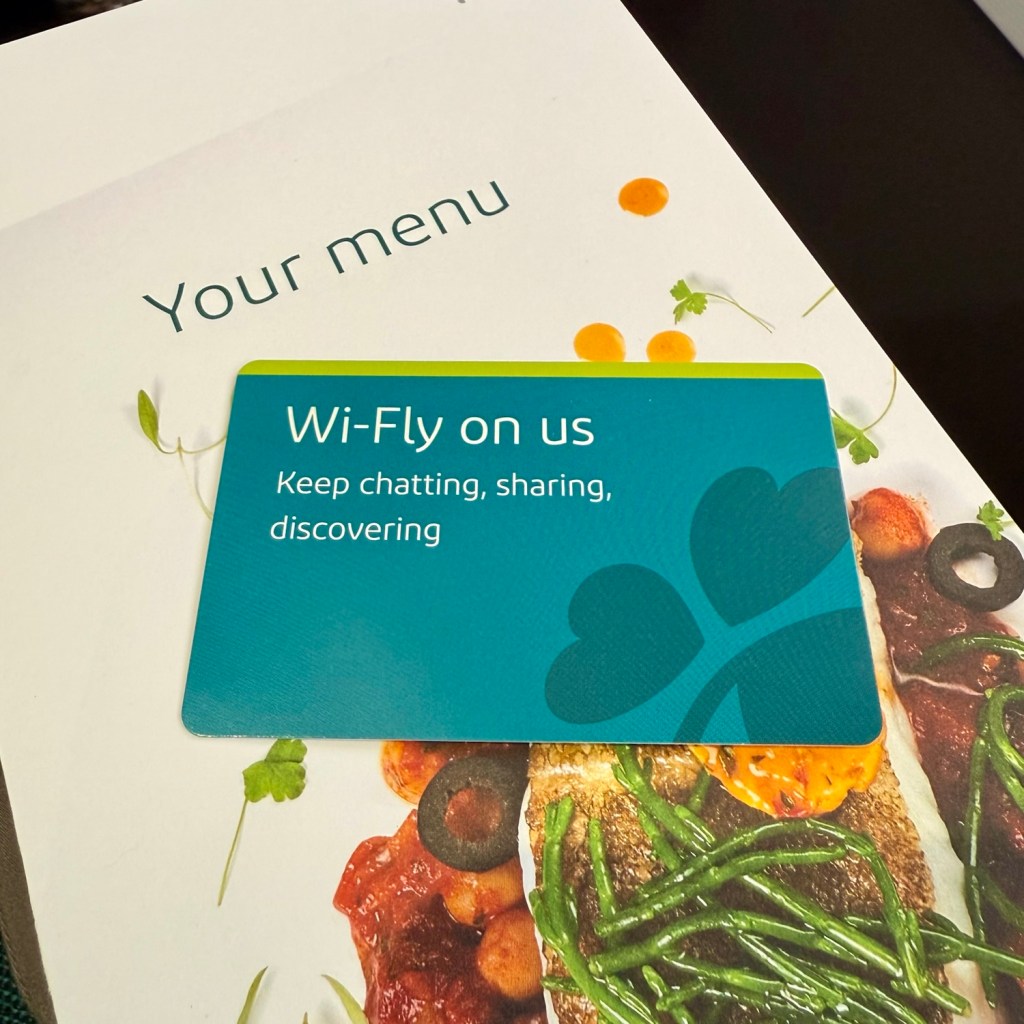 An Aer Lingus menu with a Wi-Fi access card on top, featuring colorful food images and the text 'Your menu' and 'Wi-Fly on us'.