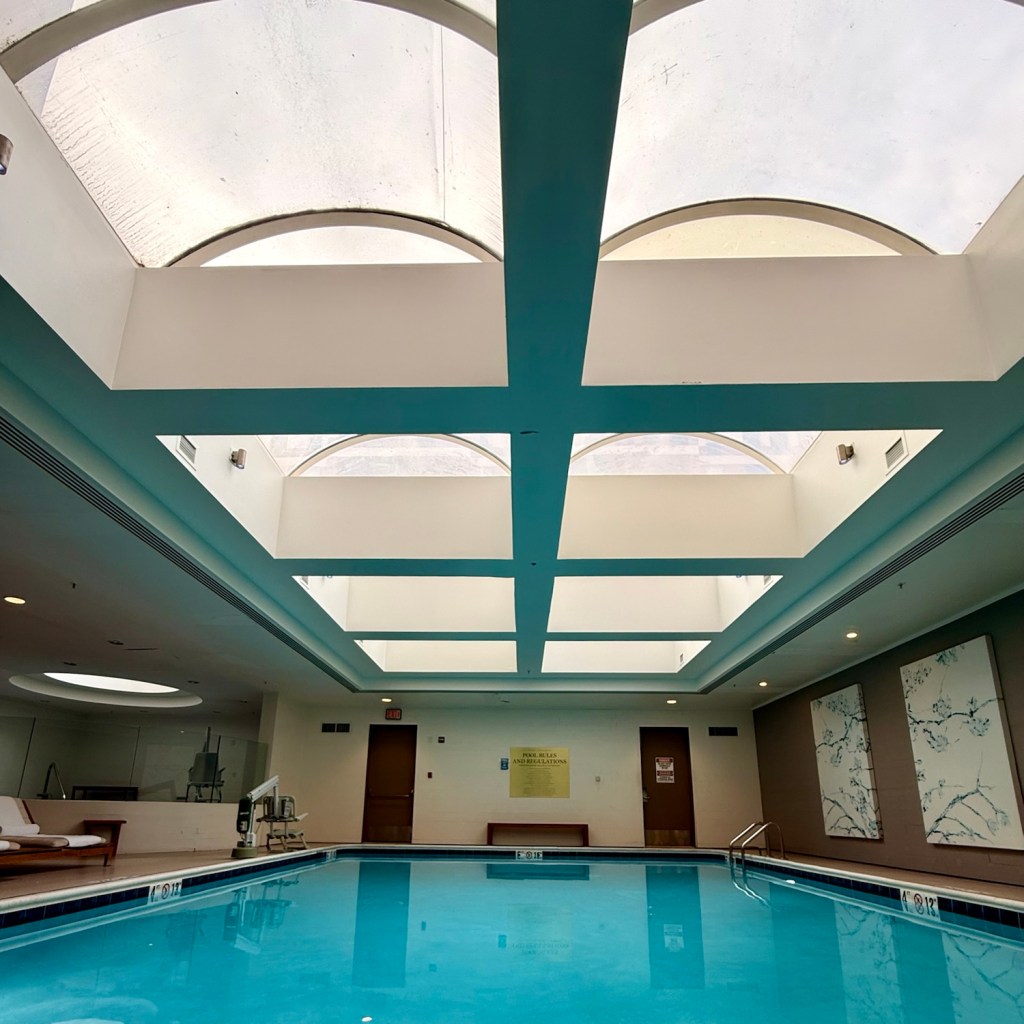Indoor swimming pool area with blue water and large skylights overhead, featuring clean lines and a calming atmosphere.