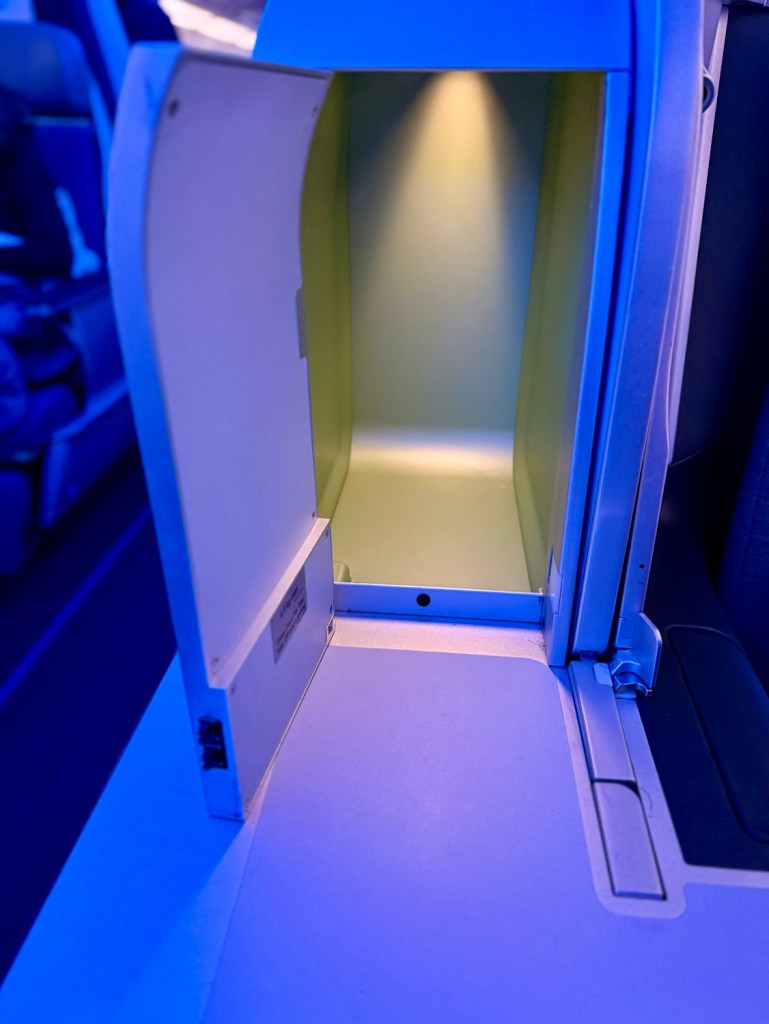 Interior view of an airplane seat storage space with soft lighting, showcasing a clean, modern design.