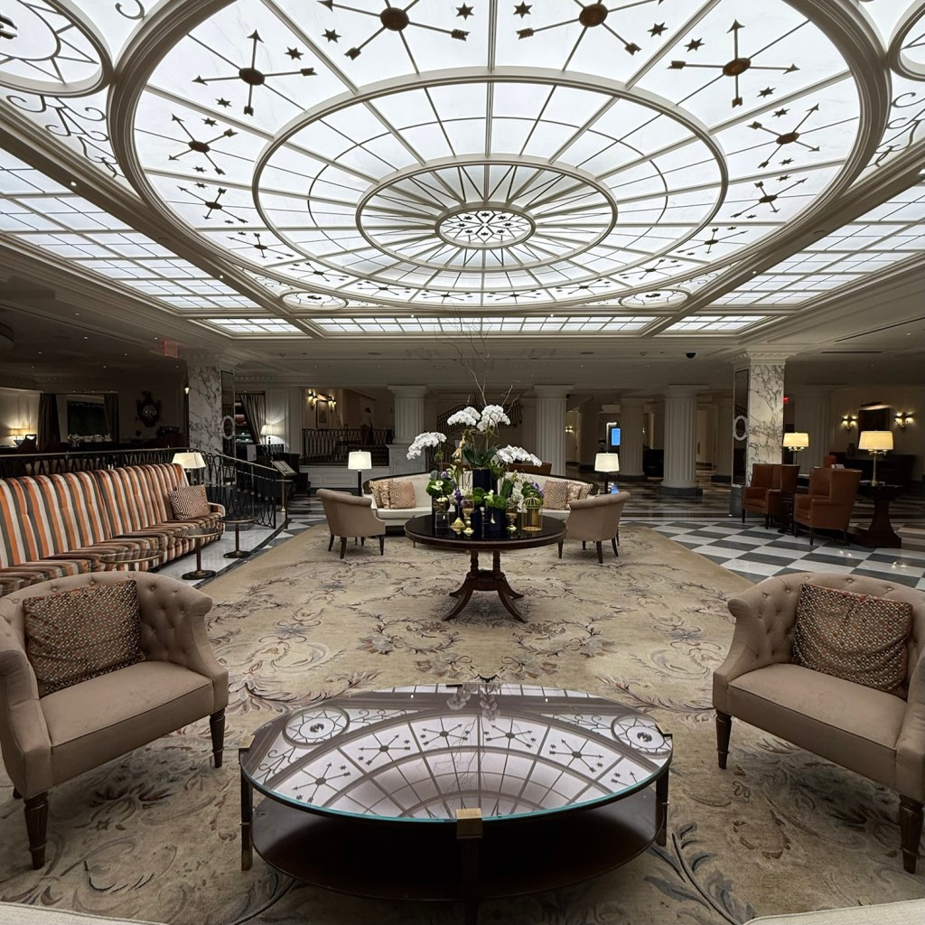 Interior view of a luxurious hotel lobby featuring ornate ceiling, plush seating, and floral arrangements.