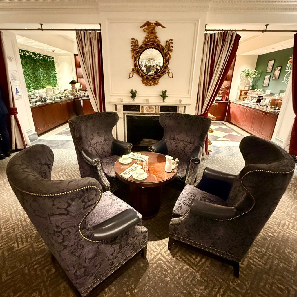 A luxury lounge area featuring elegant high-backed chairs and a round table set with tea service, surrounded by a sophisticated interior design with dark wood and decorative mirrors.