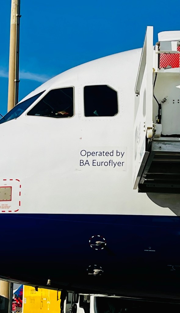 Close-up of the front of a British Airways Euroflyer aircraft showing the cockpit and jet bridge with 'Operated by BA Euroflyer' signage.