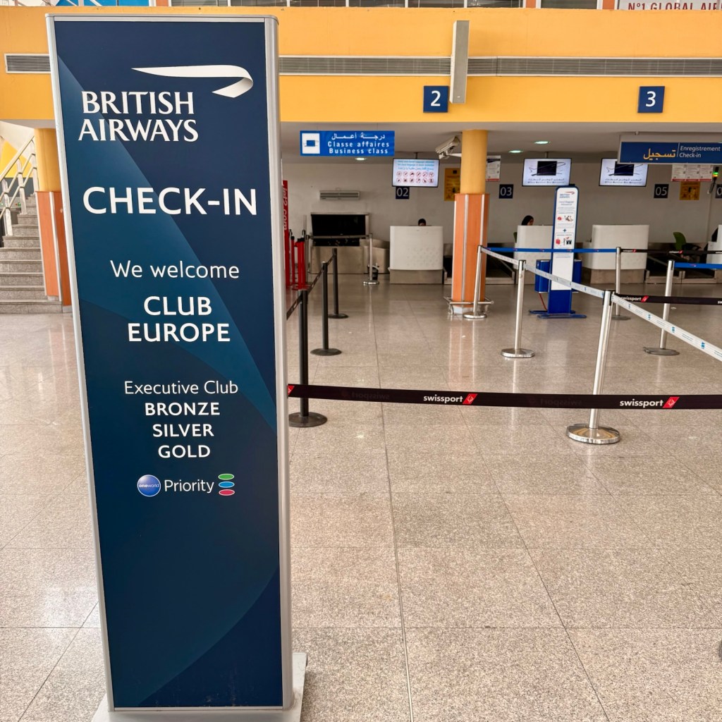 British Airways Club Europe check-in sign at Marrakech Airport, featuring priority boarding information and the Executive Club tiers.