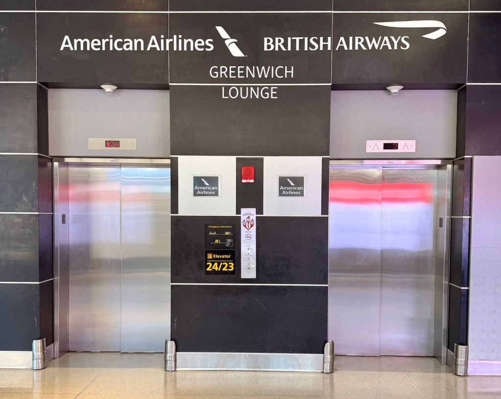 Entrance to the Greenwich Lounge at JFK Airport with signage for American Airlines and British Airways, and elevators nearby.