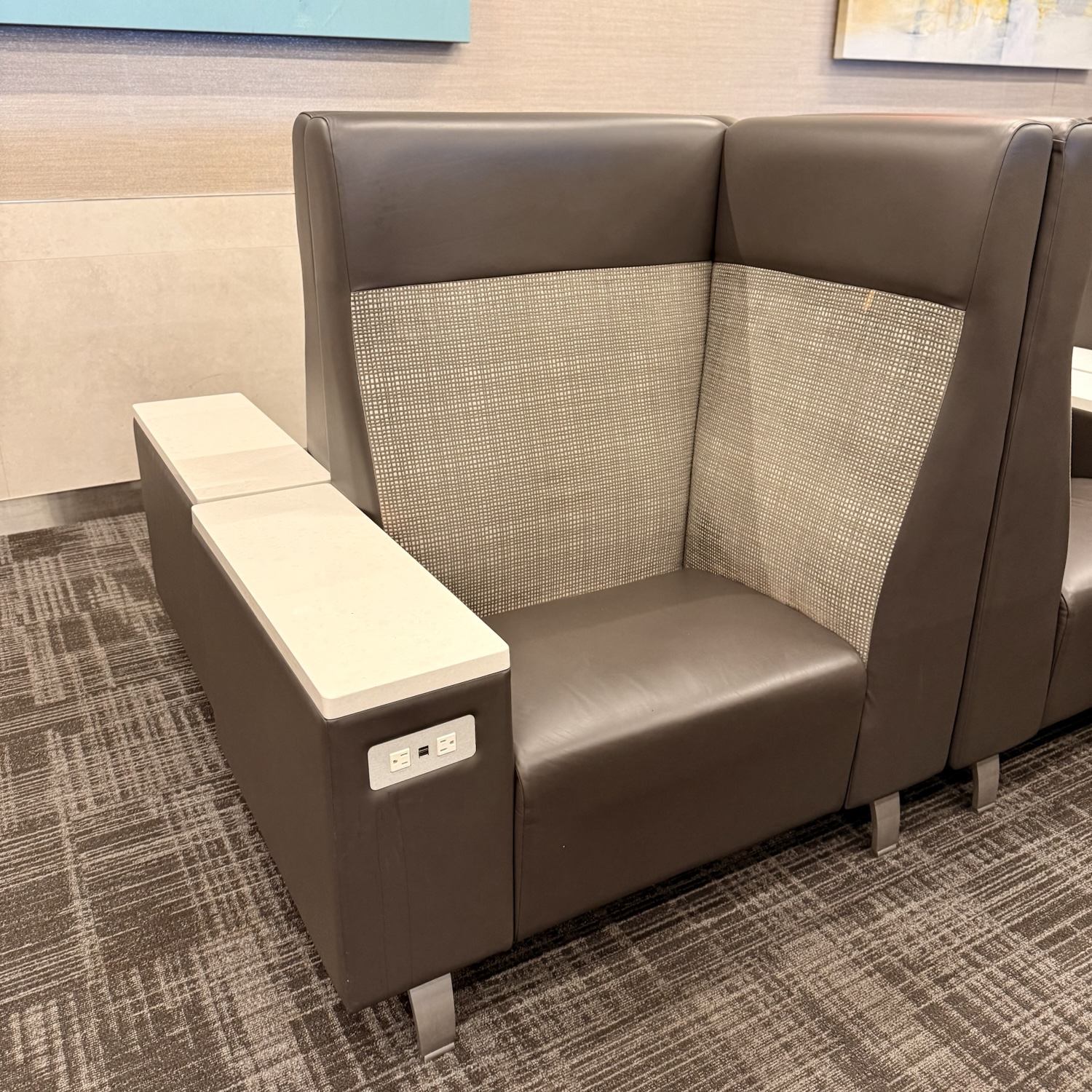 A stylish lounge seating area featuring a modern chair with a combination of leather and mesh materials, equipped with a side table and electrical outlets.