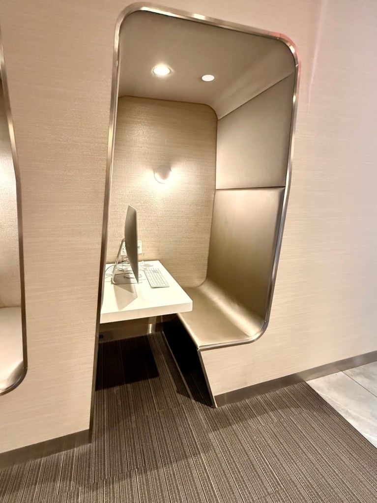 A modern work pod with a computer and keyboard inside a sleek, minimalist enclosure, featuring soft lighting and a comfortable seating area.