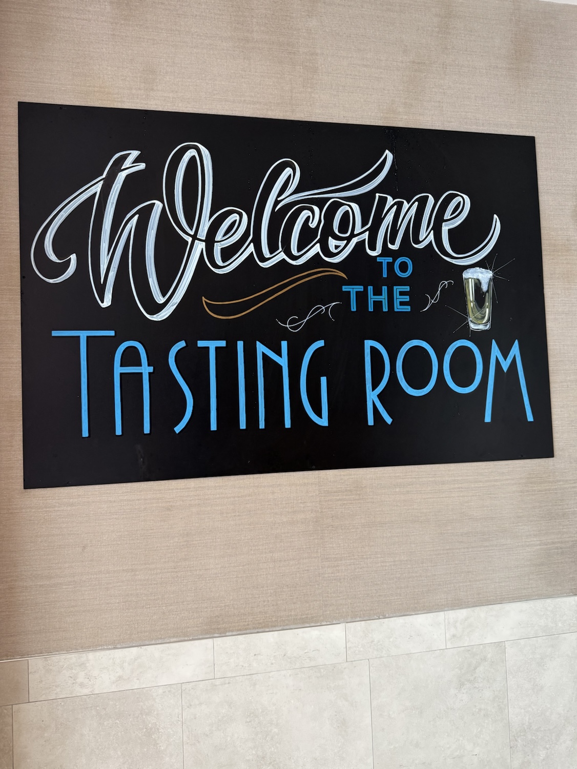 A welcoming sign for 'The Tasting Room' displaying decorative lettering and a glass of beverage.