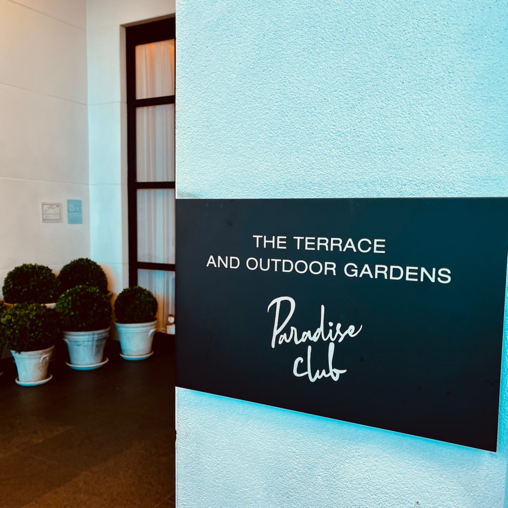 Sign indicating 'The Terrace and Outdoor Gardens' at the Paradise Club, with decorative potted plants in the background.