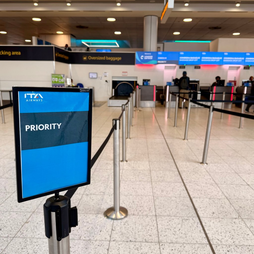 Priority check-in area for ITA Airways at the airport, featuring a sign and barriers.
