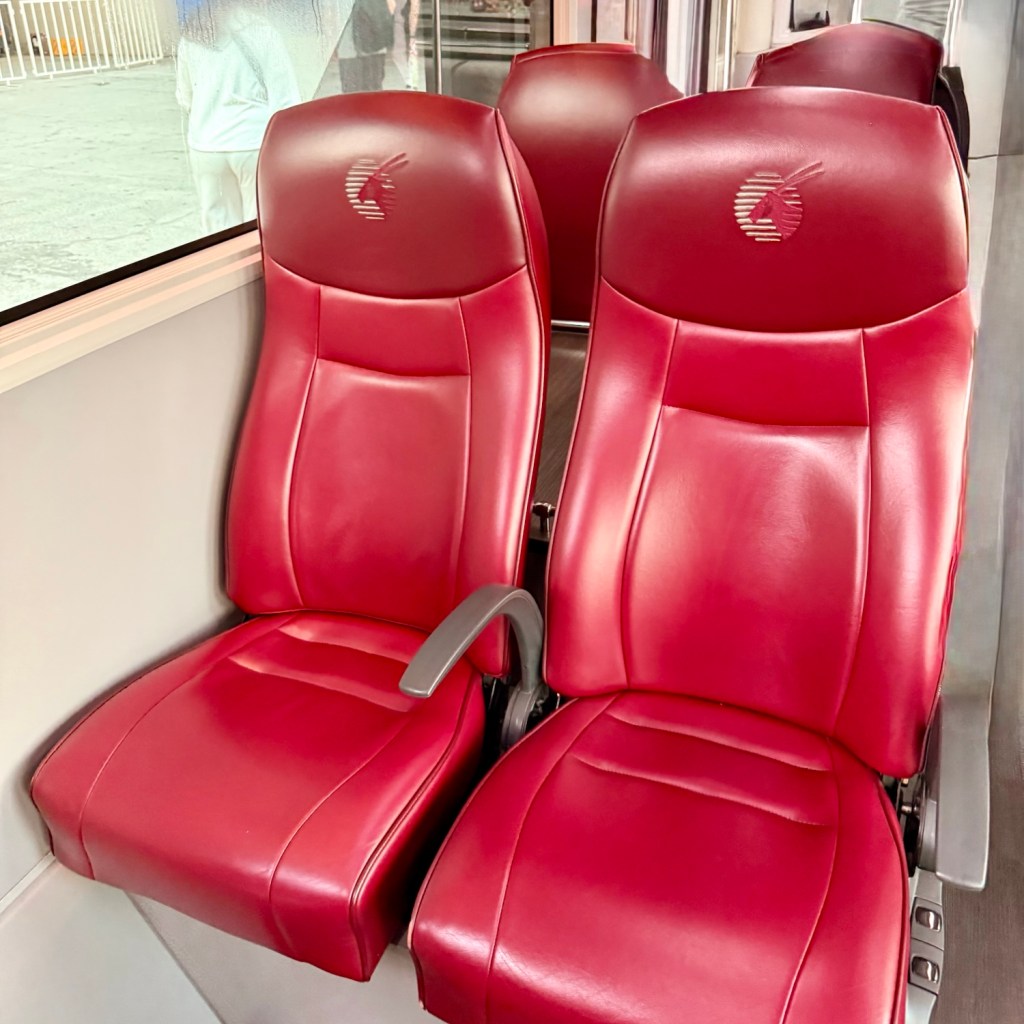 Two luxurious red leather seats with armrests, featuring an embossed logo in the center, inside a premium transportation vehicle.