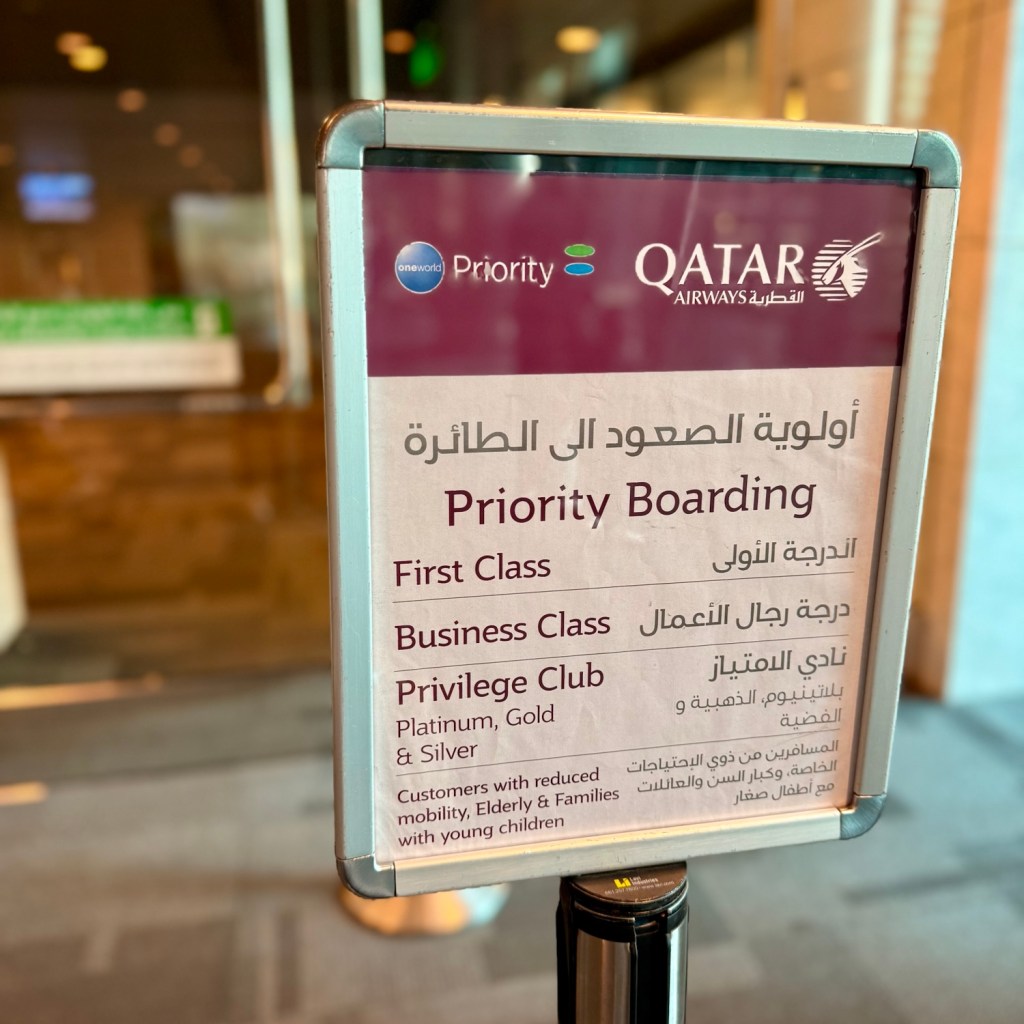 A sign indicating 'Priority Boarding' for Qatar Airways, listing categories for First Class, Business Class, and Privilege Club members.