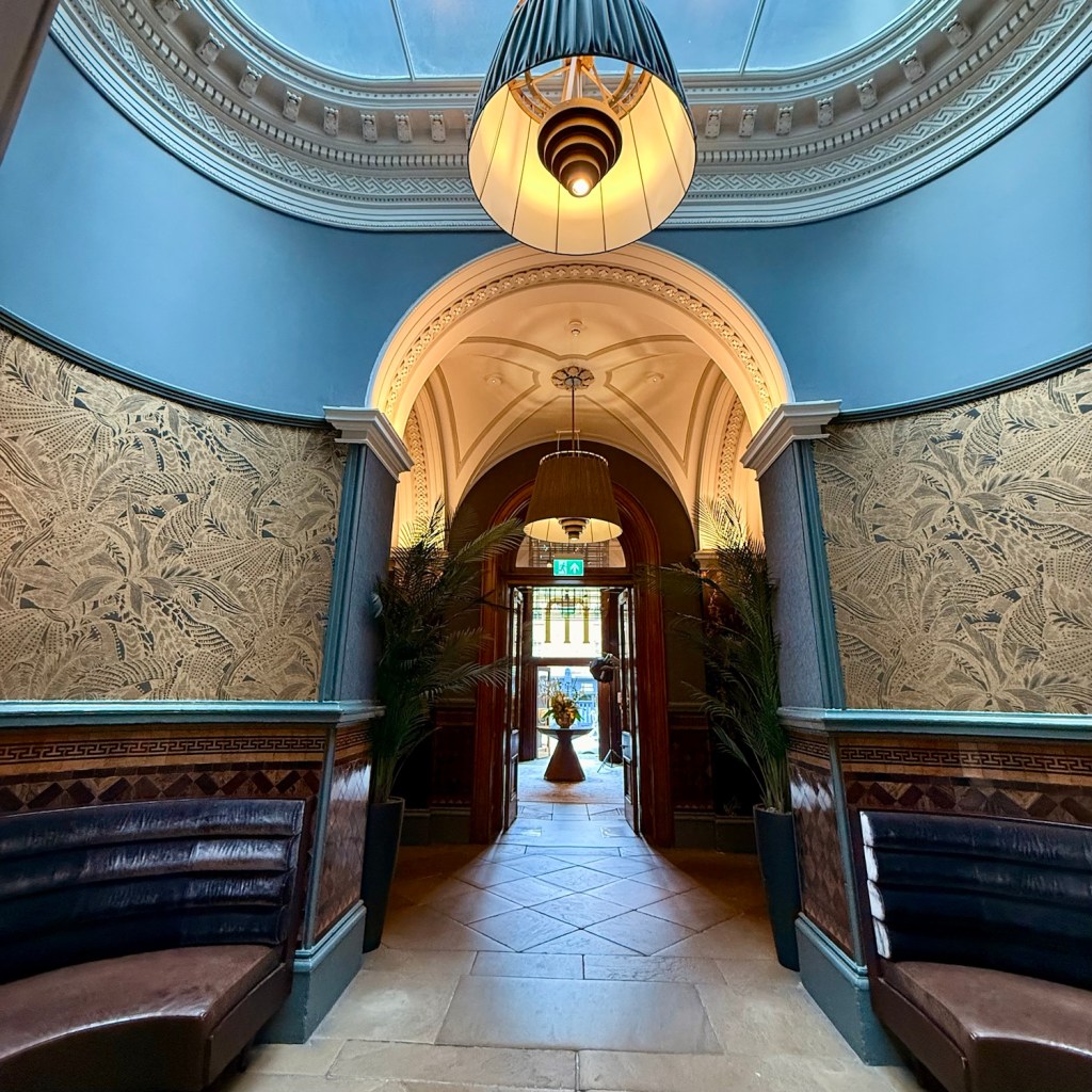 Interior view of the Municipal Hotel Liverpool, featuring elegant decor, a central light fixture, and door leading to the outside.