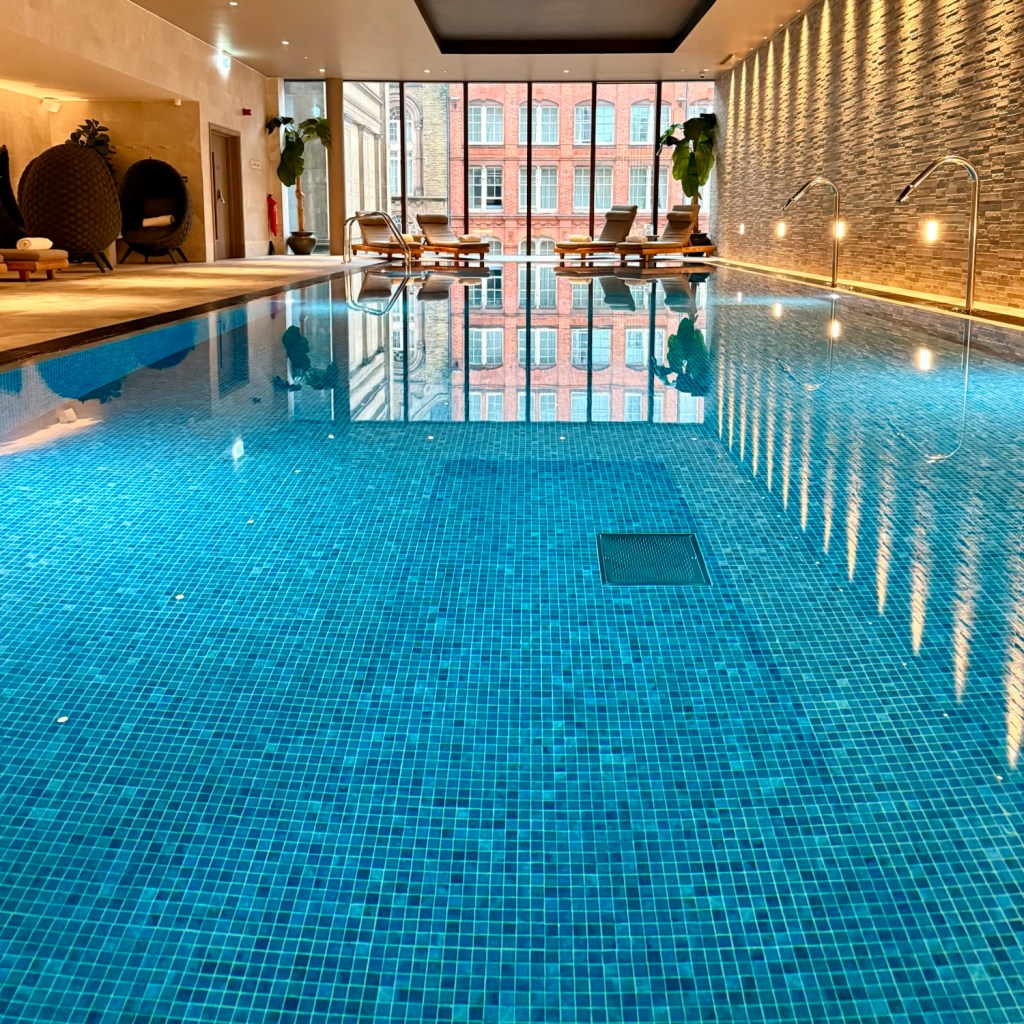 Indoor swimming pool with blue mosaic tiles, reflecting large windows and surrounding seating areas.